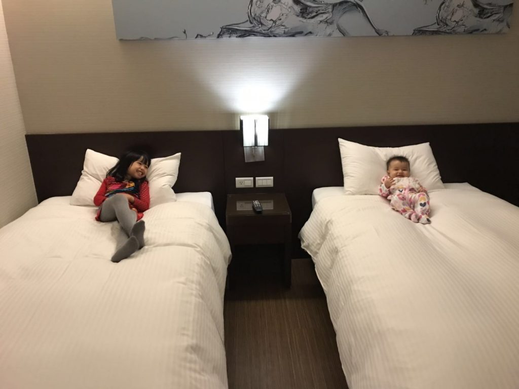girl and baby laugh in hotel bed